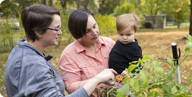 Mom's show their young son a tomato growing in the garden.